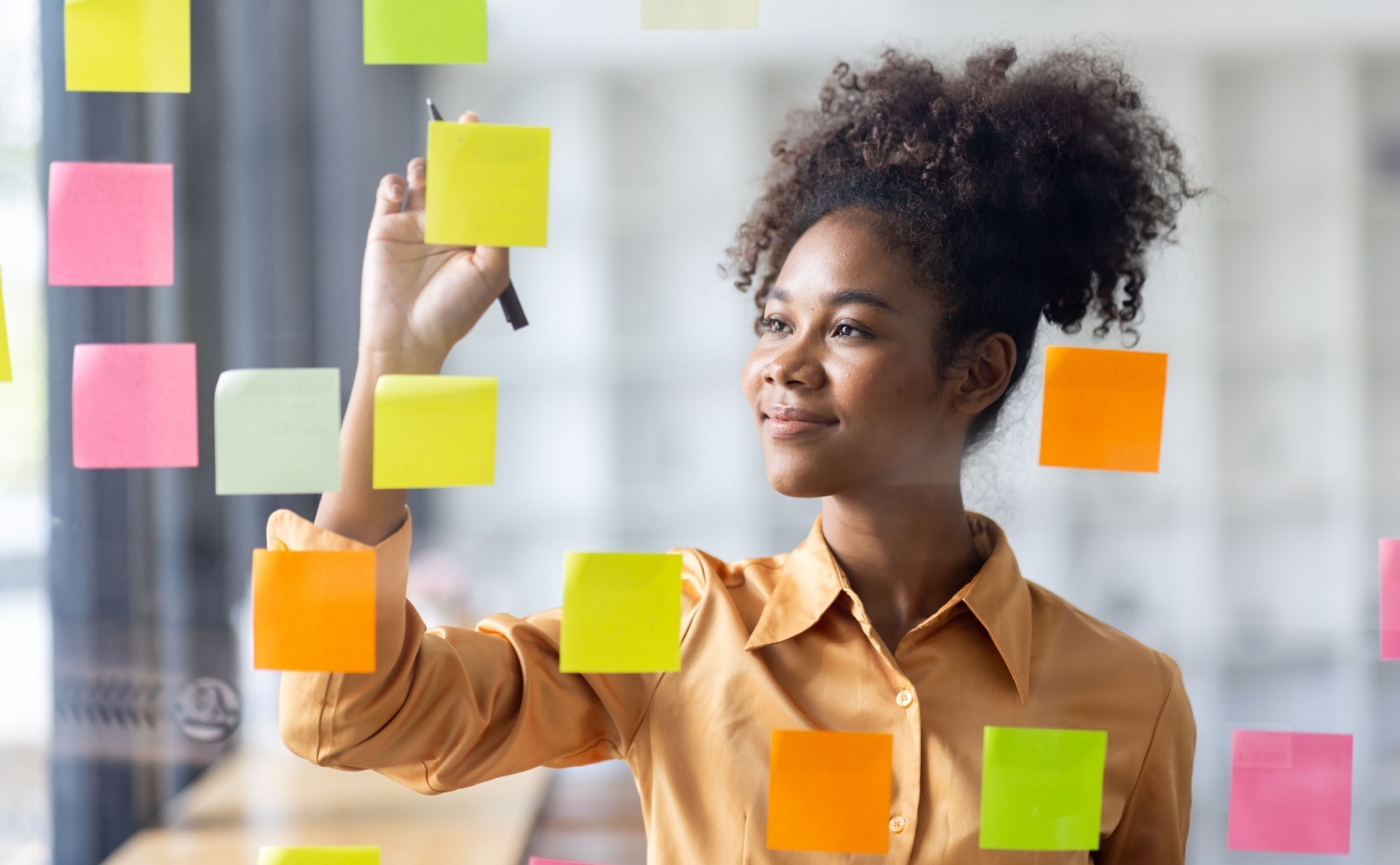 Woman writing on a glass planning board covered with sticky notes.