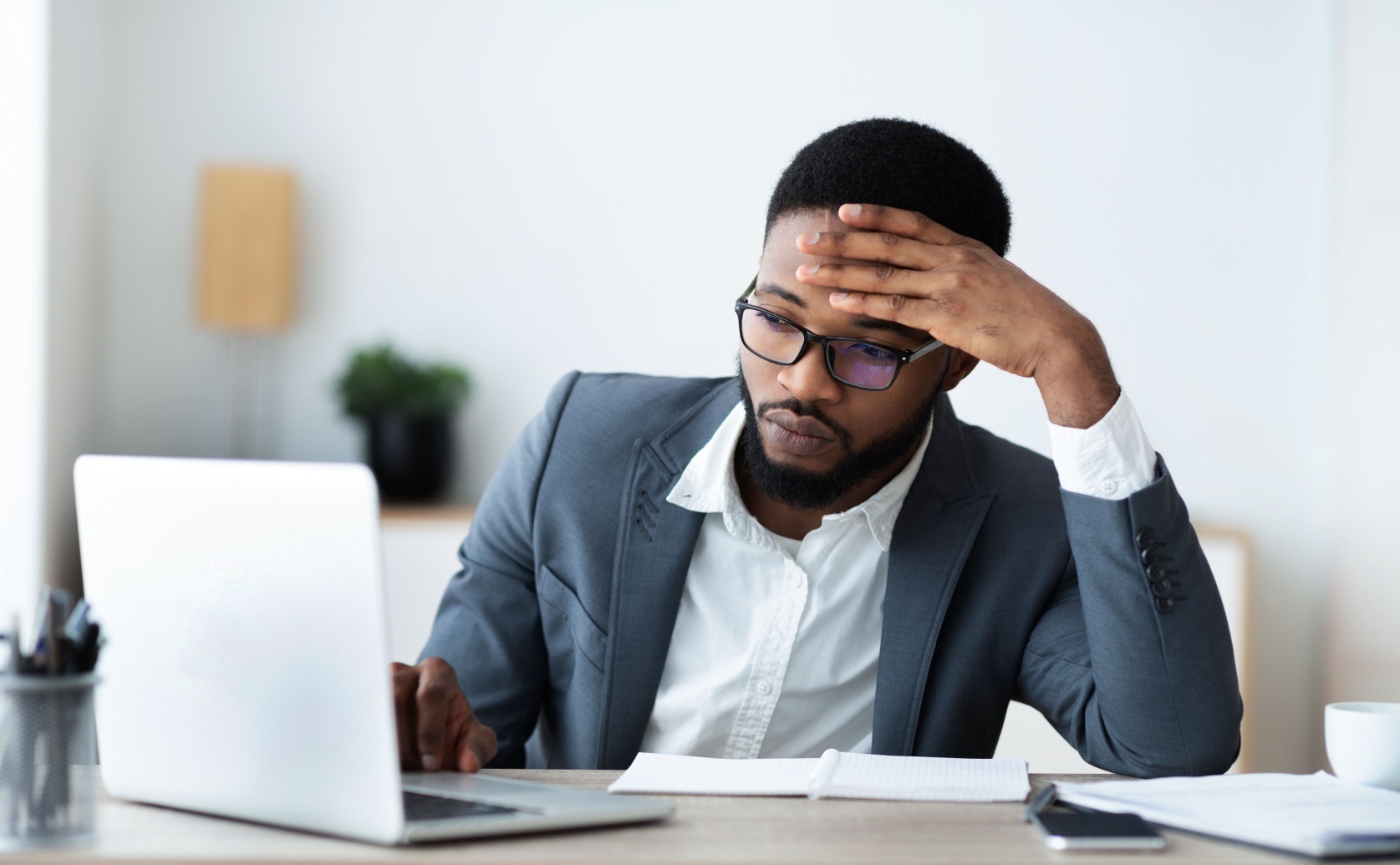Man resting his forehead on his hand while working at a laptop.