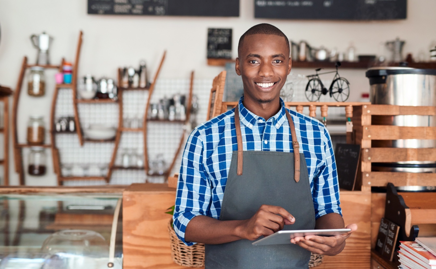Man in an apron using a tablet behind a shop counter.