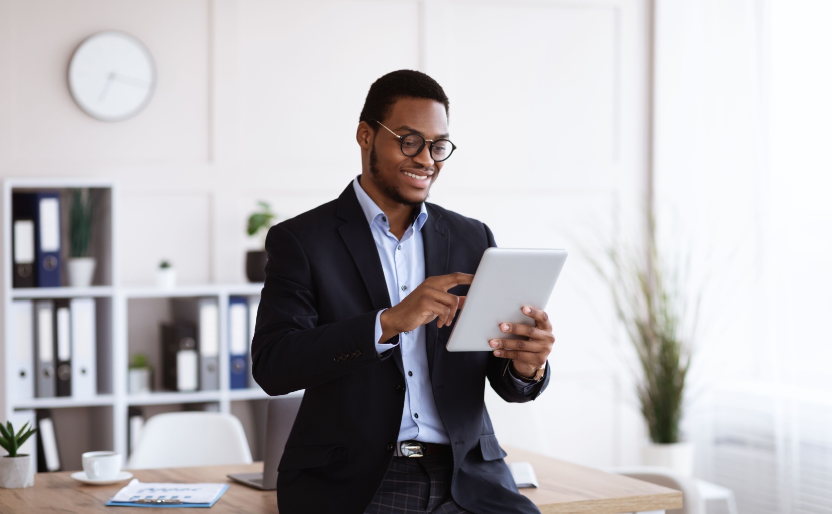 Man in a suit uses a tablet beside an office desk.