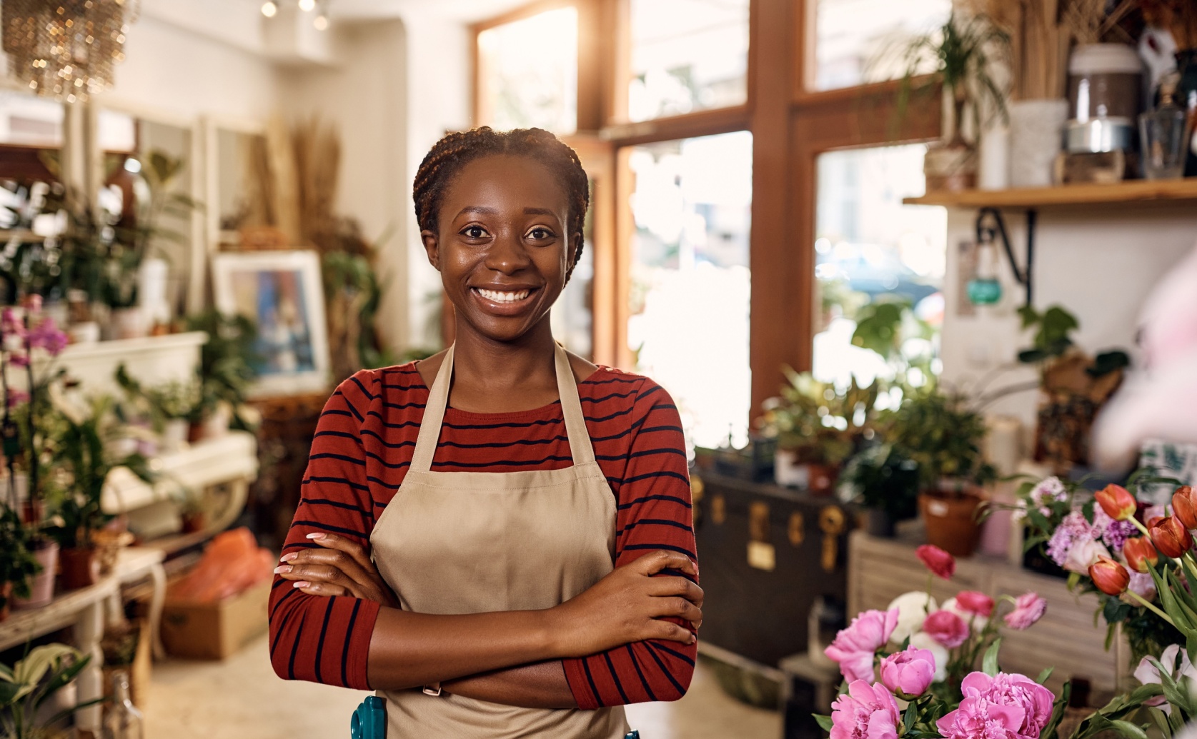 Woman wearing an apron stands among flowers in a shop.