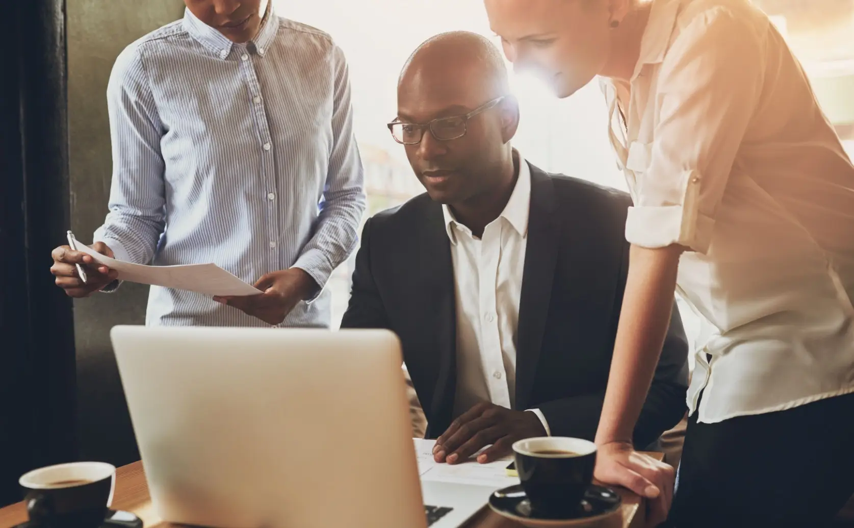 Three colleagues review a laptop and paperwork together.