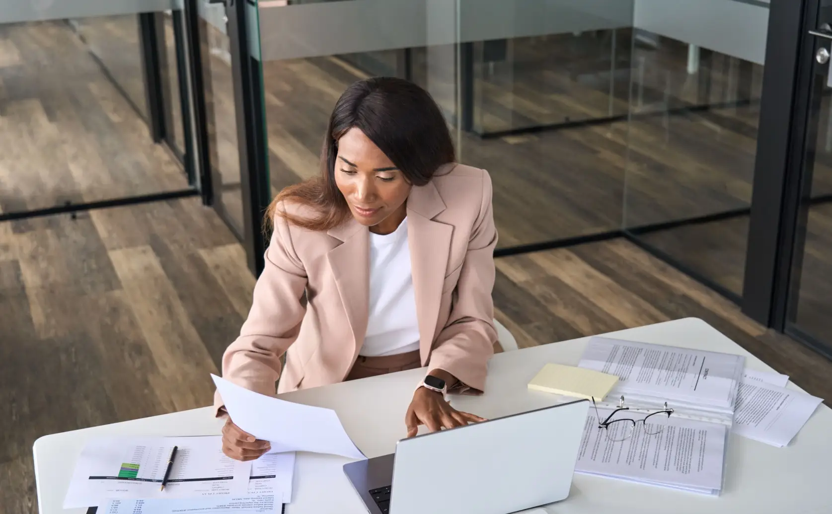 Woman reviews documents at a desk with a laptop and an open binder.