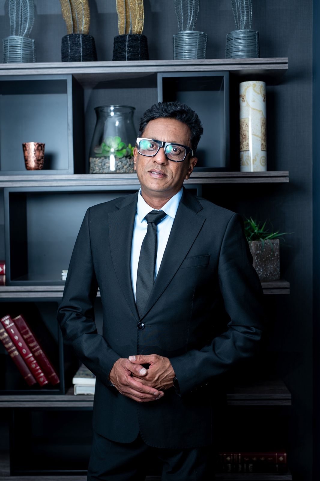 Praneshan Naidoo, founder of Fund The People, standing in a dark suit in front of office shelves.
