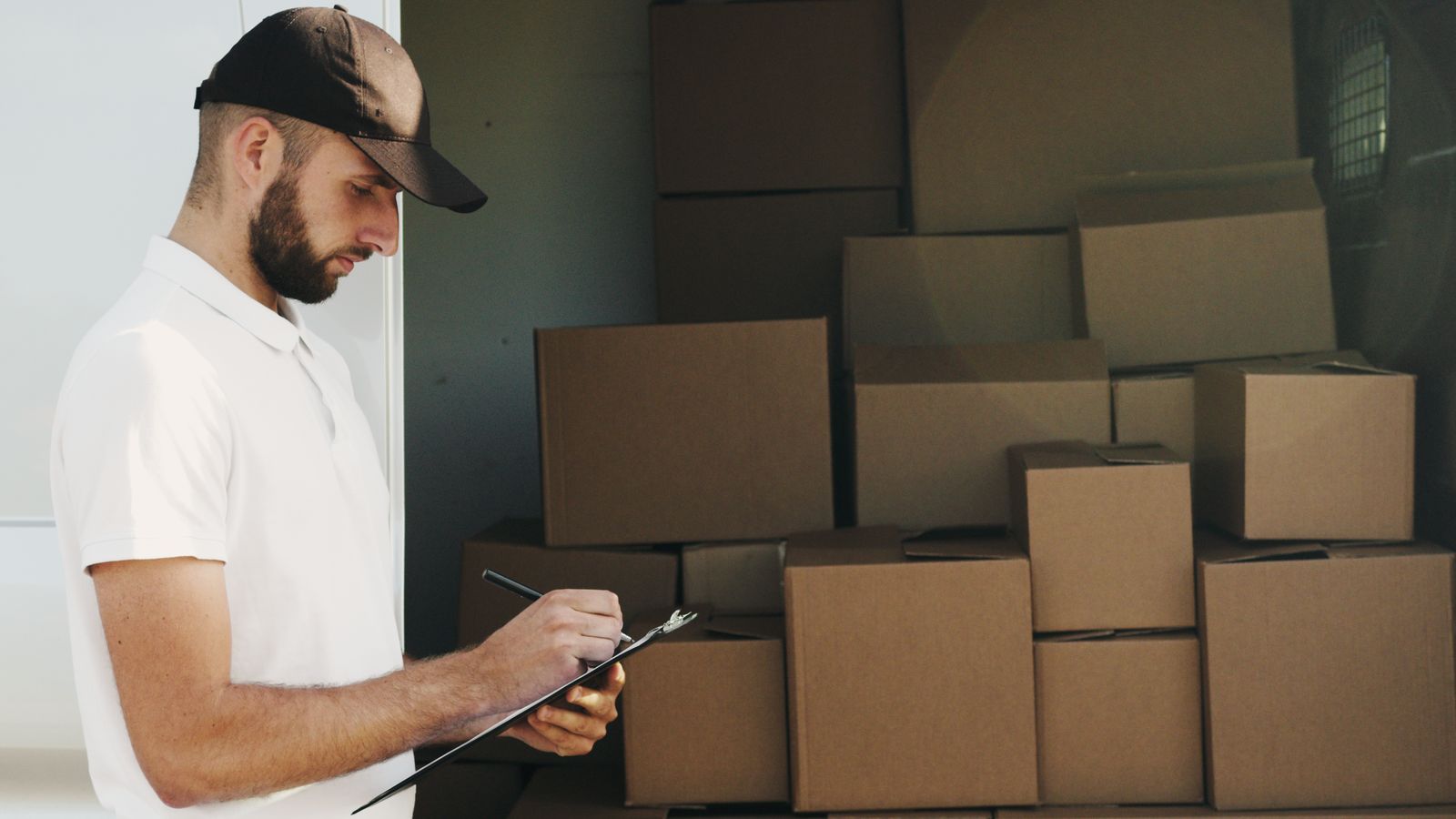 Delivery worker recording shipment details beside cardboard boxes